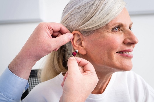 Eine Seniorin bekommt ein modernes Hörgerät eingesetzt und lächelt zufrieden.